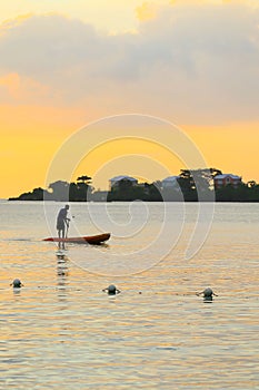 Man silhouette rowing standng on a boat at sunset time.