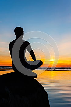 Man silhouette sitting on stone at the seaside contemplating sun