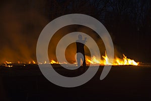 Man in silhouette tending controlled prairie burn at night