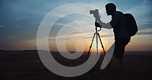 Man in silhouette using tripod for taking pictures of sunset