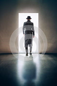 Man silhouette walking away in the light of opening door in dark