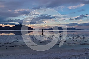 Man sillhoutte walking into sunset of lake Bonneville Salt Flats, Wendover, Western Utah, USA, America. Beautiful summits of