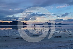 Man sillhoutte walking into sunset of lake Bonneville Salt Flats, Wendover, Western Utah, USA, America. Beautiful summits of