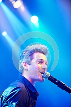 Man, singing and performing at night, music festival and stage for concert, party and entertaining crowd. Microphone