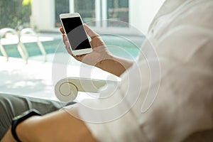 Man sit on chair near window and looking at his cell phone with swimming pool outside.