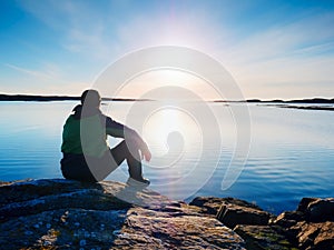 Man sit at evening sea. Hiker with backpack sit in squatting position along beach.