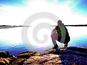 Man sit at evening sea. Hiker with backpack sit in squatting position along beach.