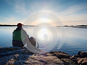 Man sit at evening sea. Hiker with backpack sit in squatting position along beach.