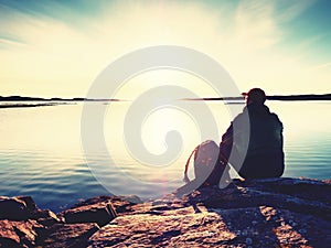 Man sit at evening sea. Hiker with backpack sit in squatting position along beach.