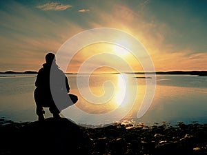 Man sit at evening sea. Hiker with backpack sit in squatting position along beach.