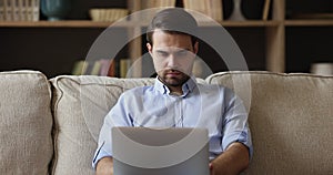 Man sit on sofa at home with laptop working remotely