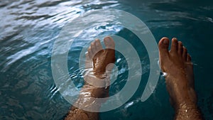 A man siting having fun splashing water from the swimming pool at hotel with his feet during the summer