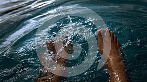 A man siting having fun splashing water from the swimming pool at hotel with his feet during the summer