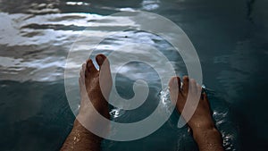 A man siting having fun splashing water from the swimming pool at hotel with his feet during the summer