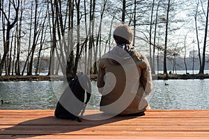 Man sits alone on a pier by the lake and thinking after hiking. Amazing nature view with lake and forest. The feeling of