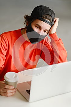 The man sits alone at a table in the open space, drinking coffee and working on his laptop. Freelance concept