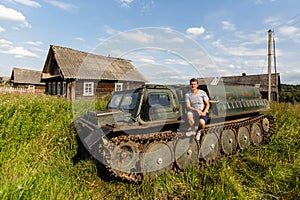 A man sits on the armor of old all-terrain vehicle in the Russian village. Nature.