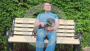 Man sits on bench and strokes smooth fur of dachshund