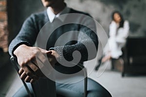 A man sits on the chair on a blurred background of his woman. Selective focus on the man`s hands. Artwork