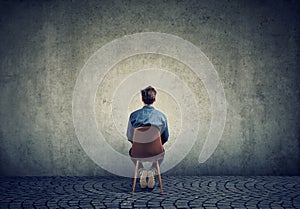 A man sits on a chair and looks at an empty concrete wall