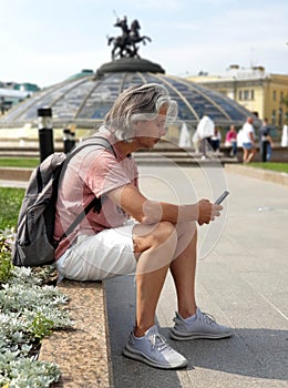 A man sits on the curb and looks into a smartphone