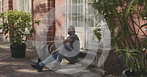 A man sits down on the porch of a brick house.