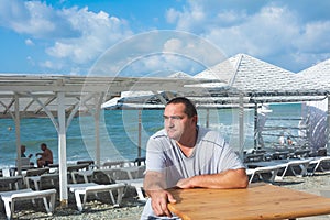 A man sits at an empty table on a sunny day in summer on the beach. Summer vacation