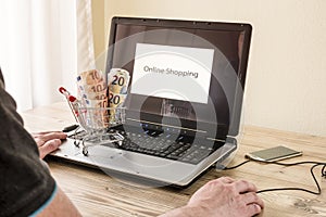 Man sits in front of laptop with shopping cart full of money