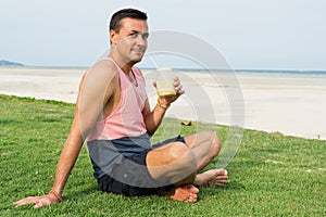 The man sits on a grass in the tropical country of the island Samui, the Man drinks smoothie.