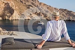 A man sits with his back on the shore of the bay and looks at the cliffs and the blue sea