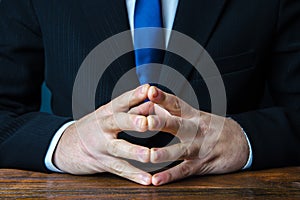 A man sits with his hands in lock. Gesture of strength consolidation and deliberation. Peace of mind and cold calculation.