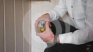 Man sits and holds glass of brown alcohol  and next to it is bottle of whiskey