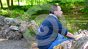 A man sits by a lake on a stone staircase between two stone ends