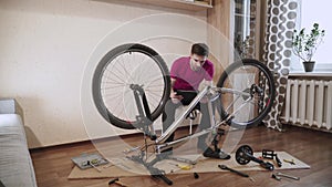 Man sits near broken bicycle in room. Upset man looks at tablet.