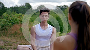 Man sits opposite woman meditating in Lotus pose in nature