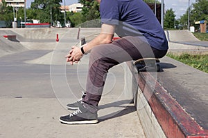 A man sits on a skateboard on the background of a skatepark. Feet close up. lifestile concept.