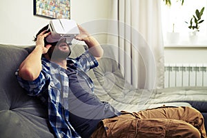 Man sits on sofa and having fun using white VR headset