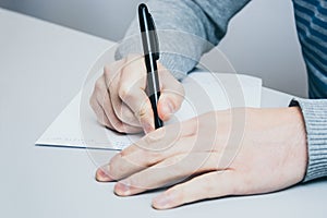 Man sits at the table and writes with a pen on paper