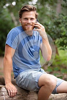 man sits on tree trunk in forest using mobile phone