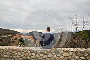 Man sits on a wall and looks at the Meteora monastery