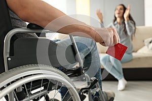 Man sits in wheelchair and holds condom in his hands opposite woman sits and happily raises his hands up.