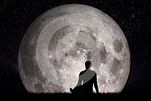 Man sitting alone on grass and looking on moon. Imagine the future concept.