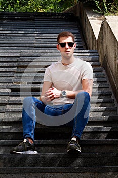 Man sitting alone on steps. Handsome boy with sunglasses. Male model posing for shooting, sitting on old stairs.