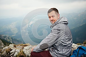 Man sitting on atop a mountain with landscape behind him