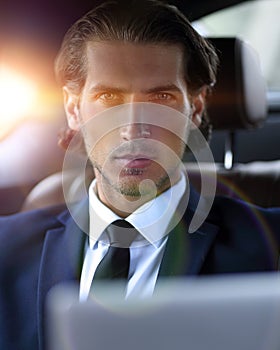 Man sitting in the back-seat of a car, using his laptop