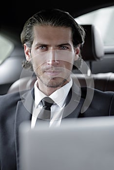 Man sitting in the back-seat of a car, using his laptop