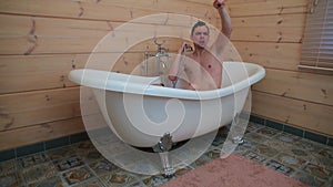 A man sitting in the bath washes his body and makes dance moves.