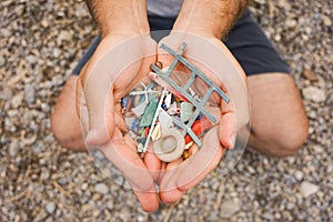 Man sitting on the beach and Holding with his two hands Plastic and Micro plastics waste and garbage from the sea and the sand.