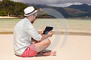 Man sitting on the beach and reading on tablet