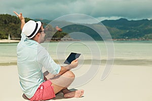 Man sitting on the beach and waving while holding an ipad